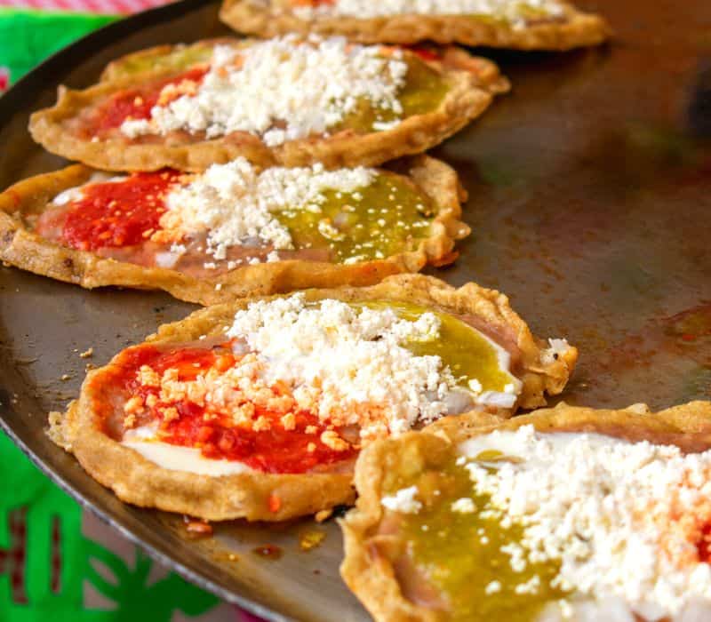 memelas with red and green salsa on a large cooking comal