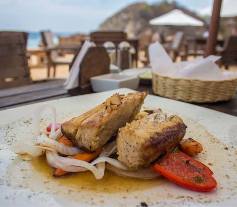 grilled fish and veggies on a plate at a beachfront restaurant